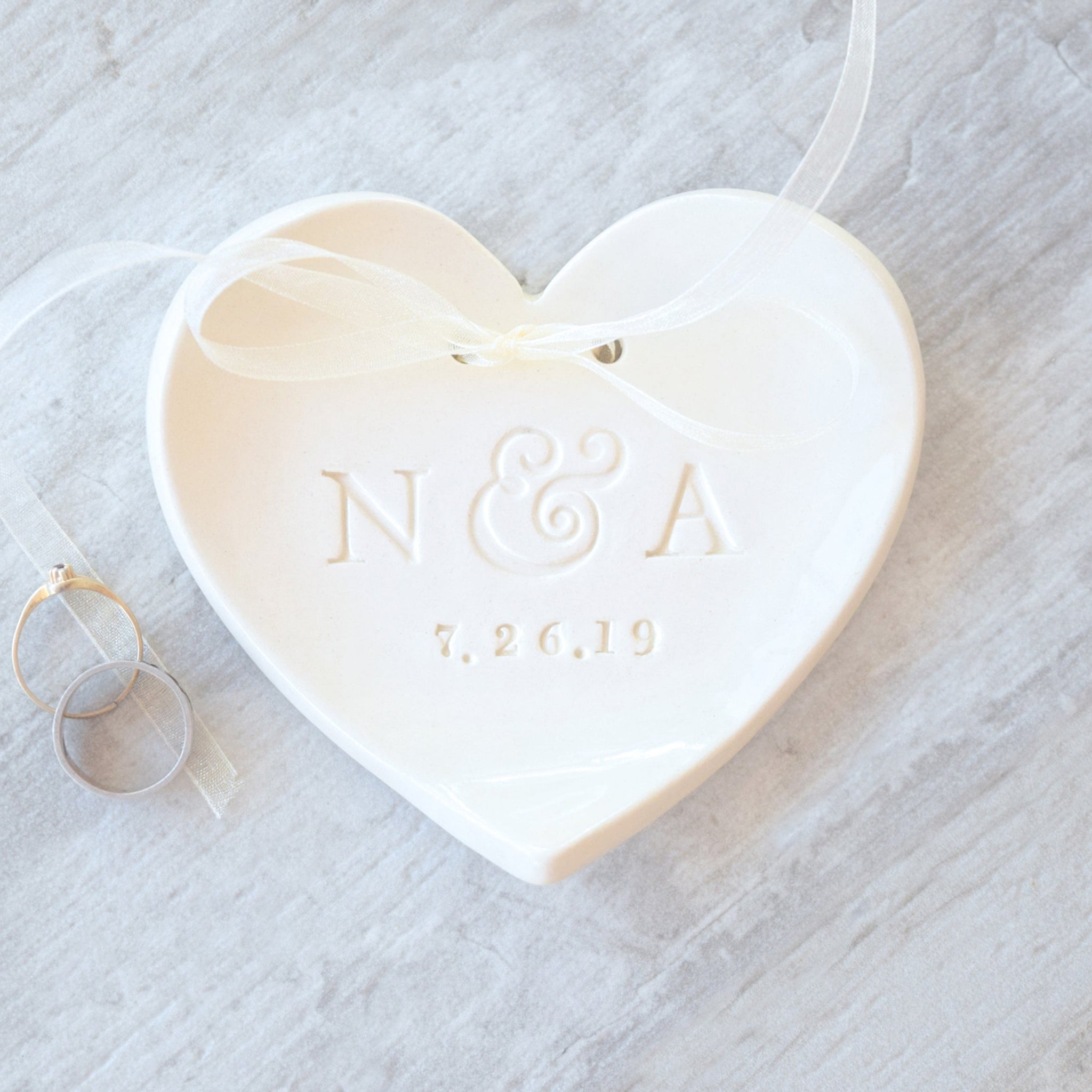 handmade ceramic heart clay plate personalized ring dish with typographic design & ribbon to hold rings on wood surface. Ideal ring bearer pillow alternative wedding ceremony keepsake. Unique bridal shower gift future daughter in law present.