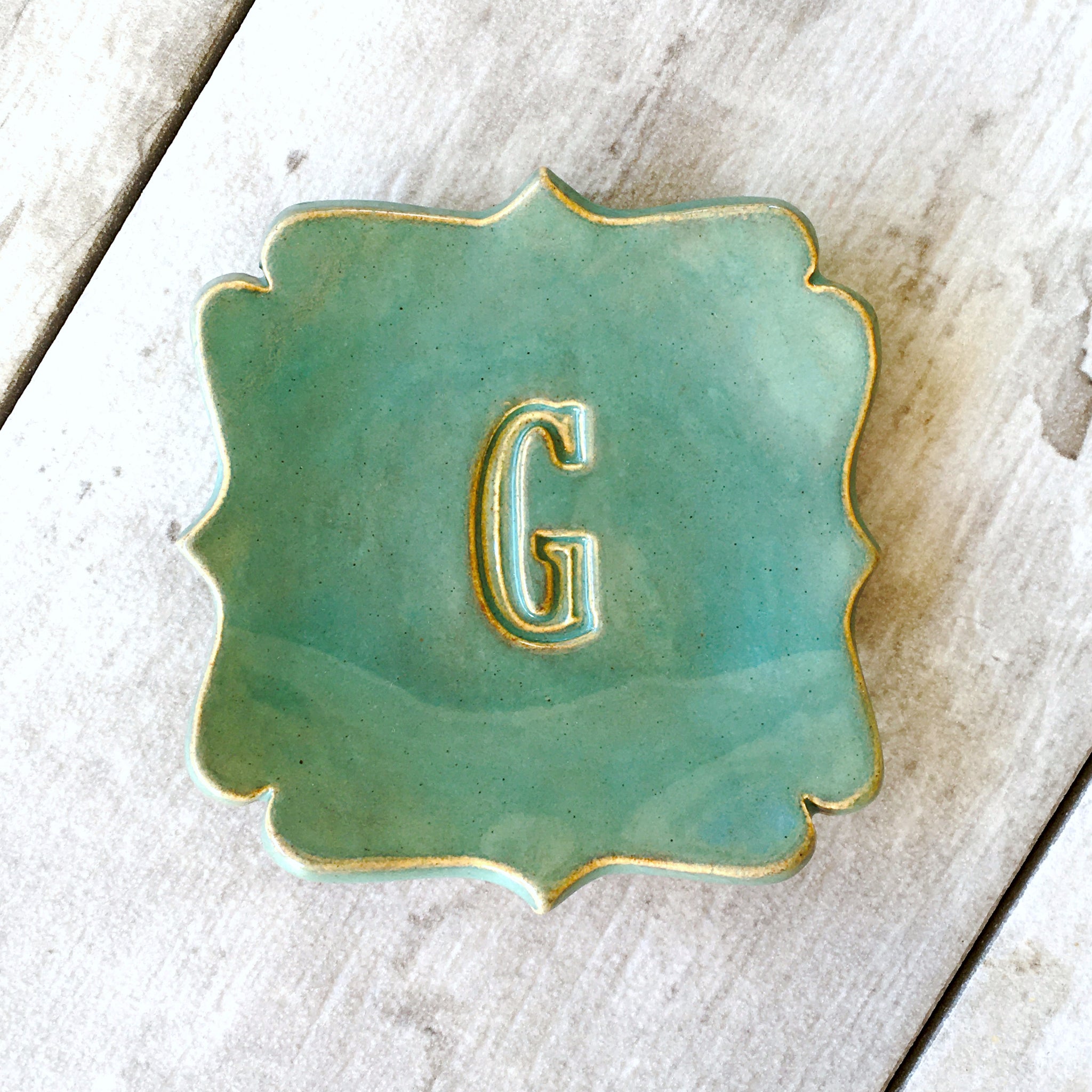Handmade ceramic curvy square tray in Rustic green gloss with golden rim edge & large letter 'C' pressed in clay, dish on a wood surface. Personalized pottery spoon rest each artist created with your choice of hand engraved big name name letter & optional date, farmhouse kitchen utensil holder, curvy corner square ceramic tray gold tone letter & rim accent 