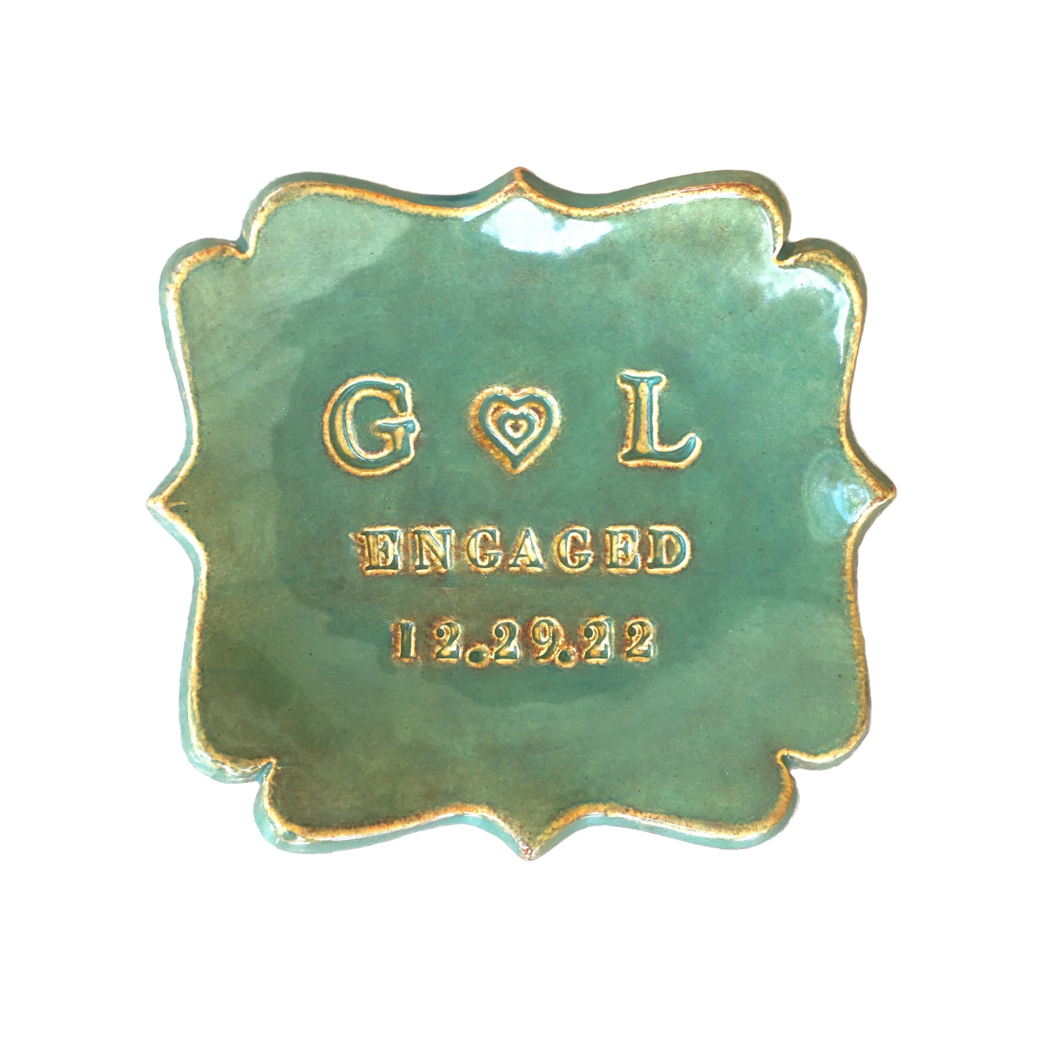 handmade ceramic abstract square ring dish personalized jewelry holder in rustic green and gold glaze on white surface. Typographic design includes a heart between 2 name initials, the word engaged & date. Modern farmhouse home decor tray. Unique engagement ring dish for engaged couple party gift and wedding rings tray for married anniversary keepsake. Ideal military wedding gift.