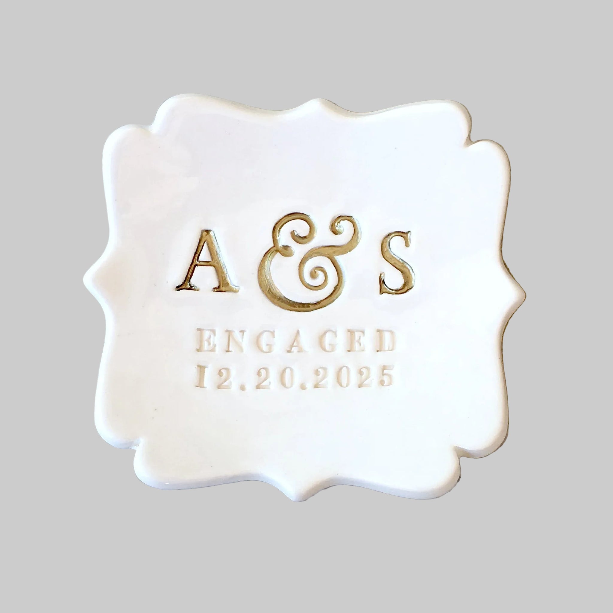 handcrafted ceramic abstract square tray with curvy sides and typographic design on gray surface. Country cottage chic modern farmhouse white gloss personalized ring dish engagement ring holder with pressed name initials, the word engaged and a date. Monogram letters are painted gold. Ideal engaged couple gift, bride to be keepsake for future mrs daughter in law. Tabletop decor jewelry storage for bracelets, earrings, necklaces.