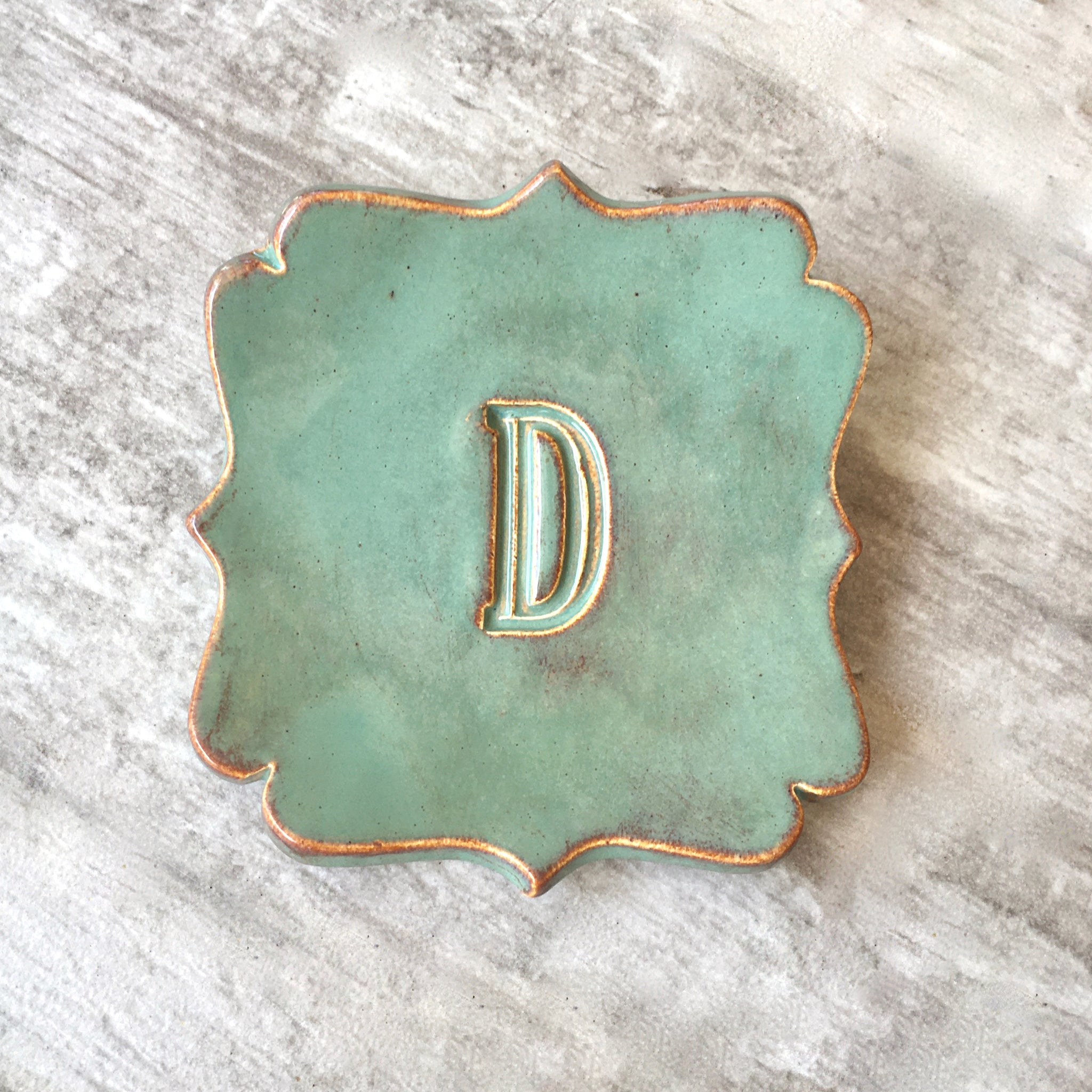 A scalloped ceramic monogram dish in a golden green glaze with rustic gold rim and a pressed letter 'D' in the center, photographed on a rustic whitewashed wood surface. Handmade ceramic curvy square tray personalized pottery spoon rest each artist created with your choice of hand engraved big name name letter & optional date, farmhouse kitchen utensil holder, curvy corner square ceramic tray gold tone letter D
