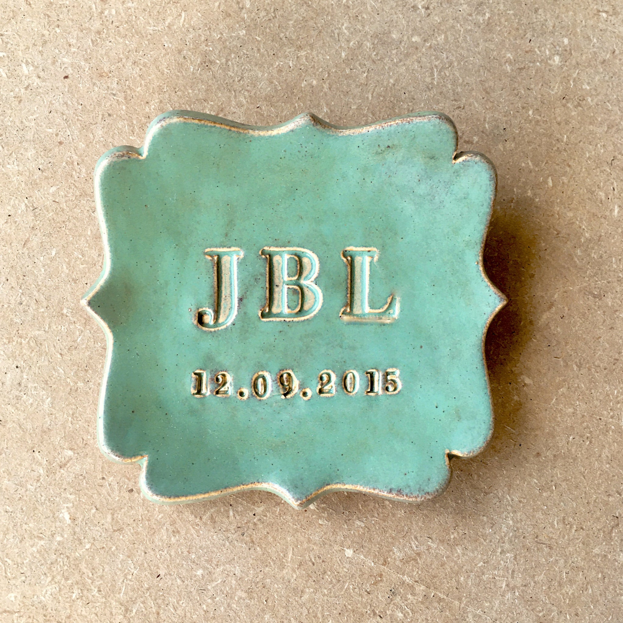 Handmade ceramic abstract shaped square tray with smooth surface, green glossy marbled finish, gold rim and typographic design on wood surface. Personalized monogram ring dish with 3 name letters and a date pressed in clay. Unique wedding ring holder commemorative plate for couple marriage ceremony, ideal anniversary gift. bespoke newlyweds keepsake, mans ring holder, graduation gift or retirement souvenir. Perfect for outdoors nature lover and military family friends.