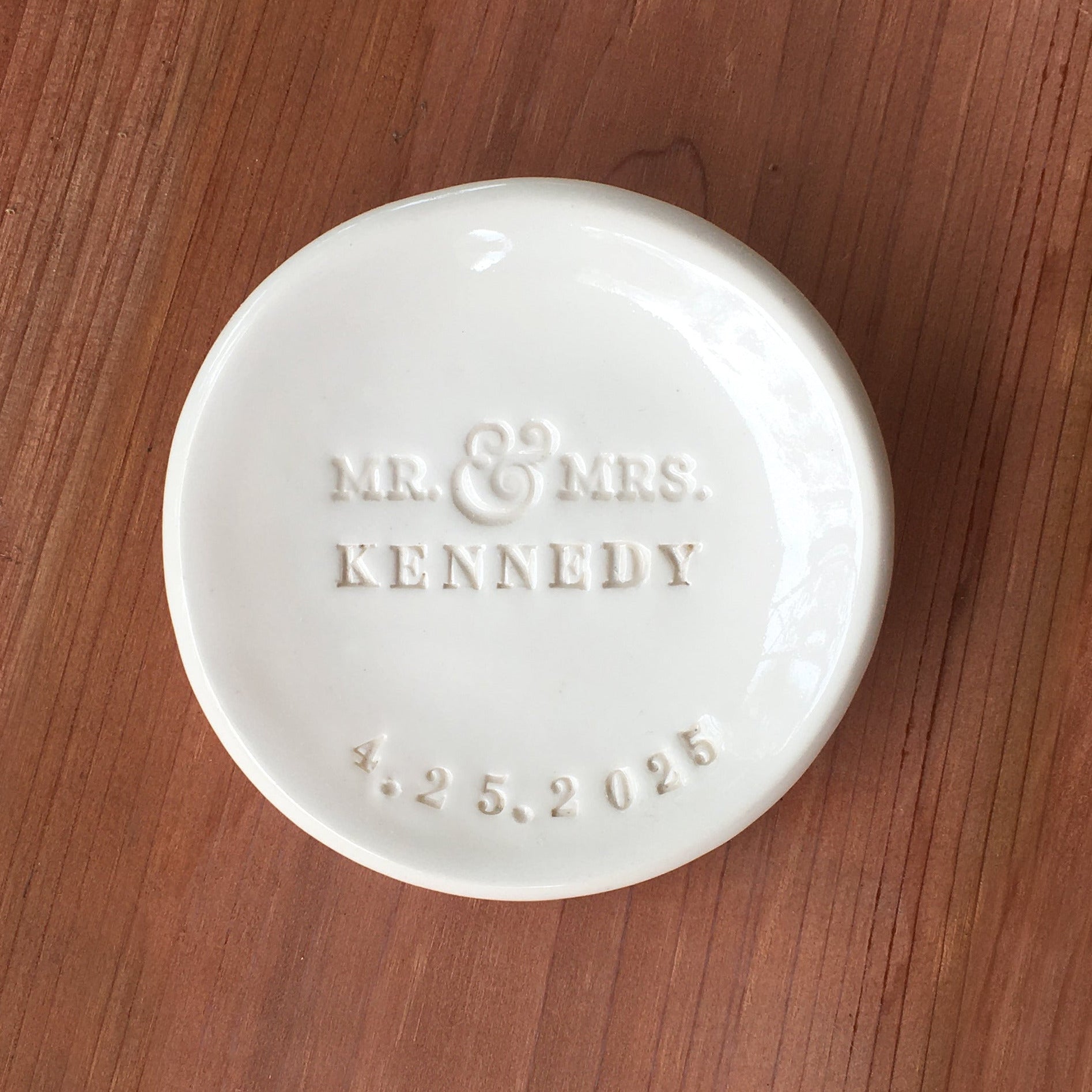 classic white handmade ceramic clay bowl personalized ring holder that is hand stamped with Mr & Mrs, your last name and a date. Dish on wood surface.