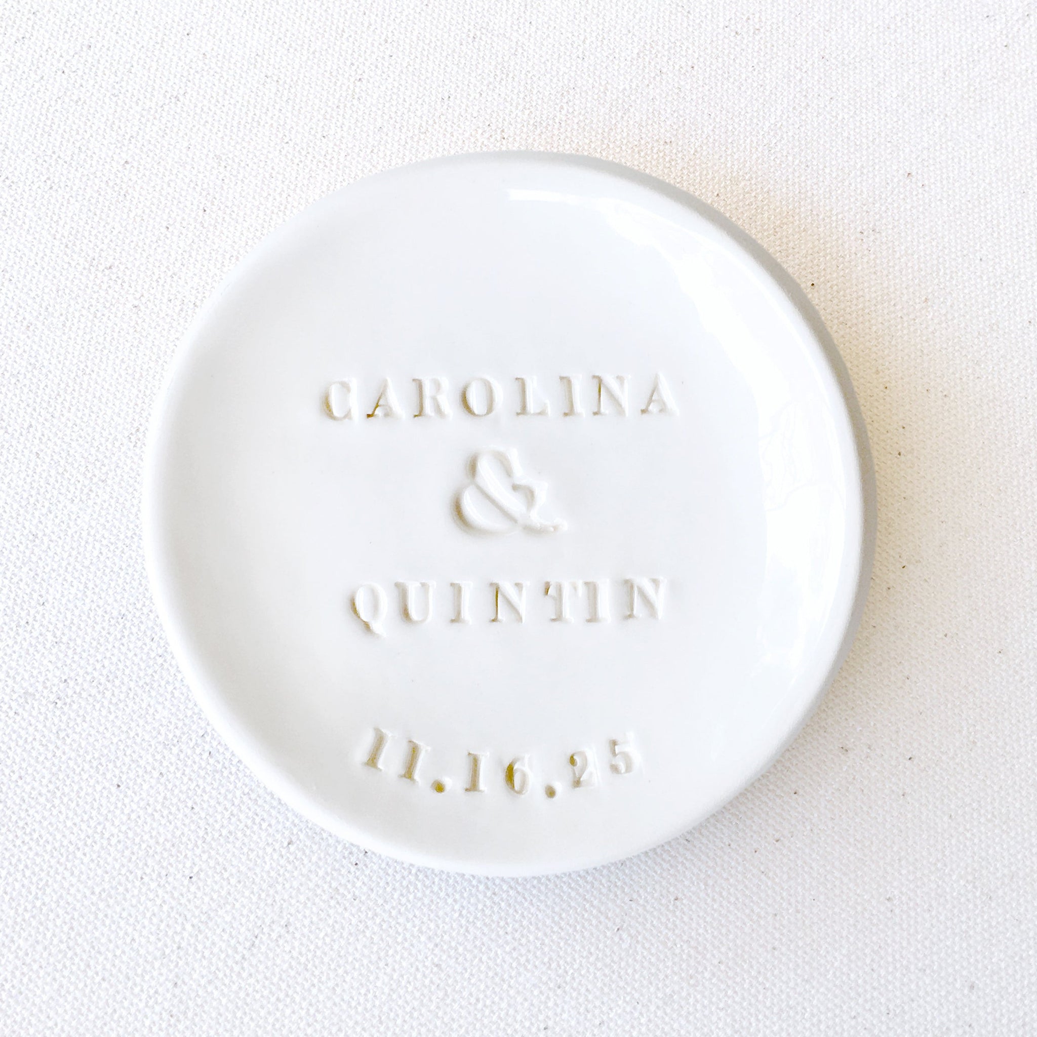 Handmade White stone ceramic bowl, personalized ring holder wedding rings dish on a white canvas surface. customized engagement gift with 2 hand engraved names and a date, jewelry storage for earrings, bracelets, necklaces.