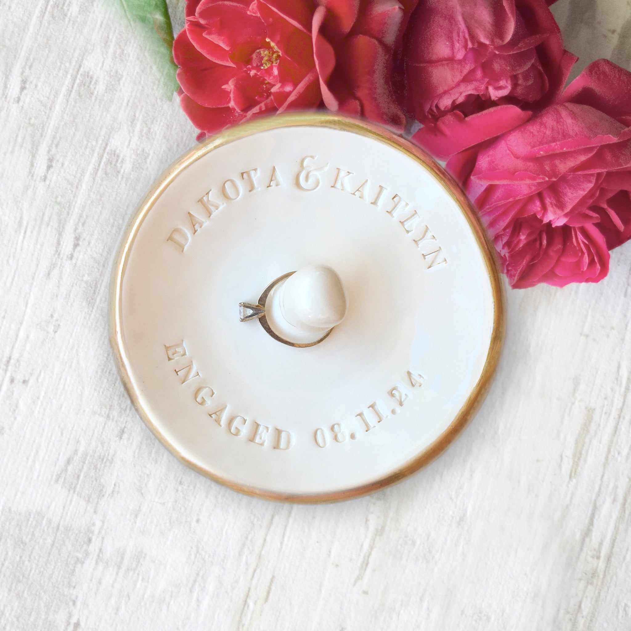 wheel thrown pottery handmade ceramic white glossy bowl with gold trim, custom engagement ring dish with center jewelry post, includes hand engraved names, the word engaged and date, newly engaged couple gift, wedding anniversary keepsake, fiance proposal mementos