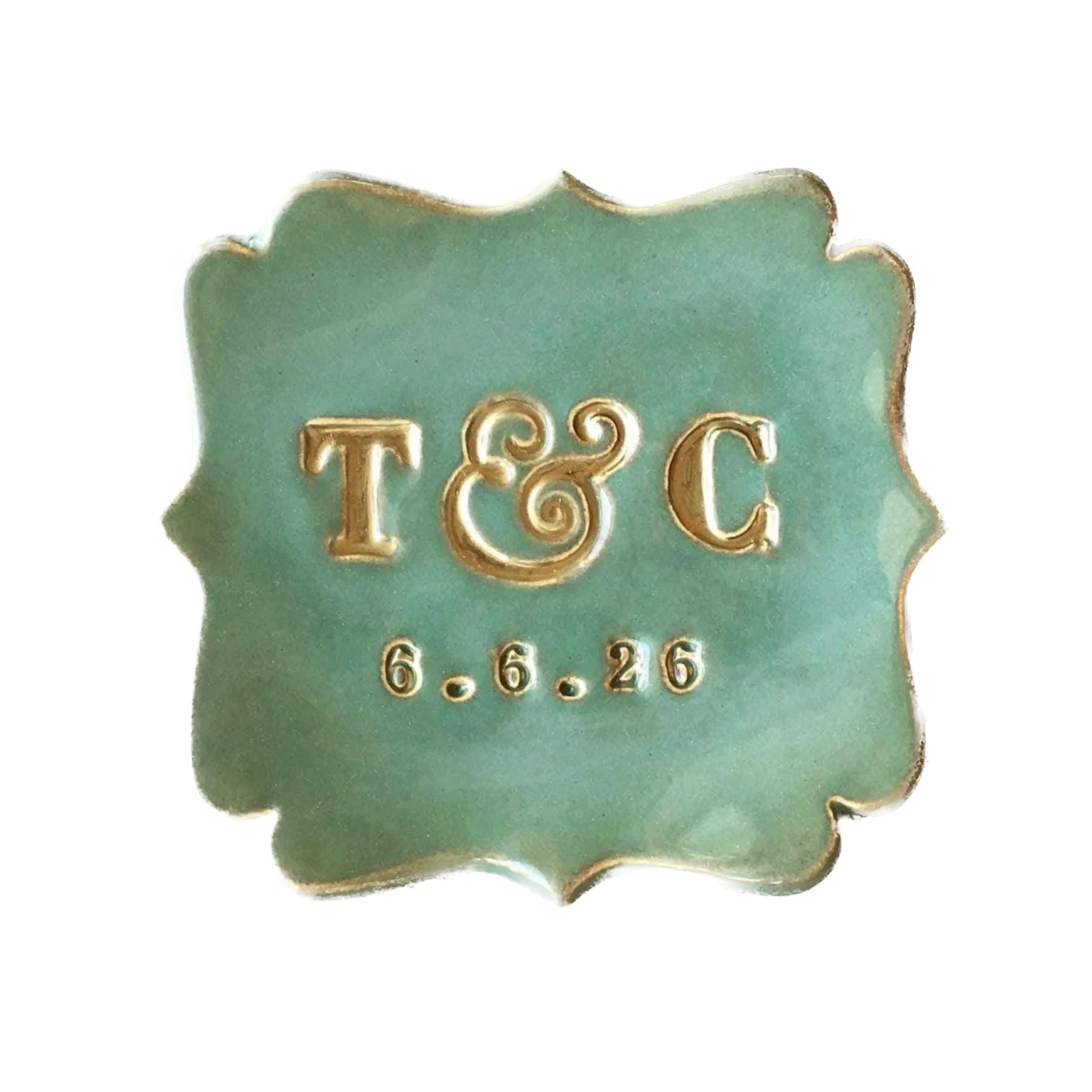 Handmade ceramic green square monogram tray with typographic design has scalloped curvy sides and gold rim accents. Dish is on white surface, Personalized wedding ring dish includes hand pressed clay: 2 name initials and a date. Initials are painted gold. Customized couple anniversary plate, jewelry holder, weddings keepsake.