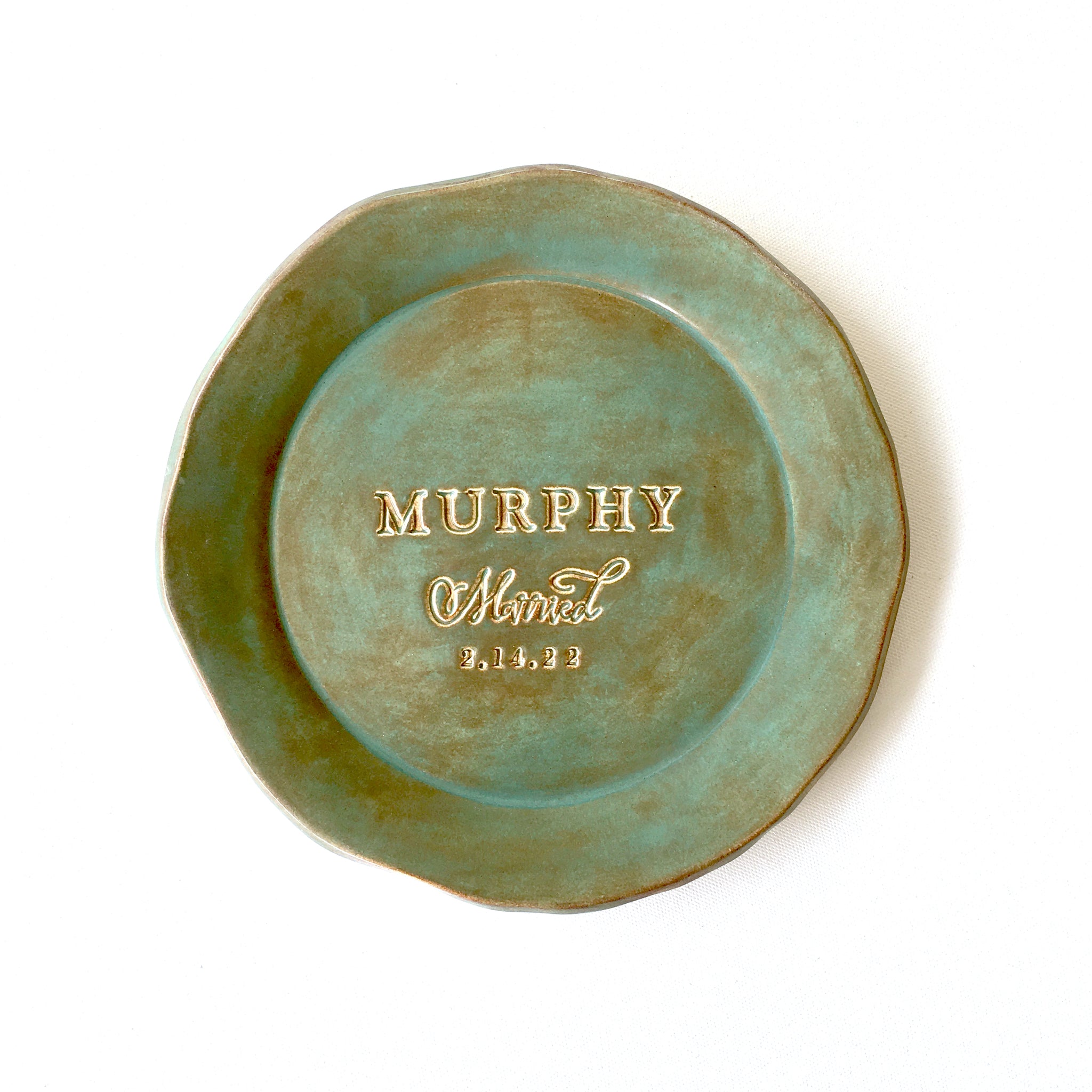 handmade ceramic rustic green round 9 inch platter. Gloss glazed personalized pottery plate unique wedding anniversary gift for couple, ceremony plate keepsake with hand engraved family last name, the word married and a date, golden brown accents on trim and gold lettering. Dish shown on a light canvas surface.