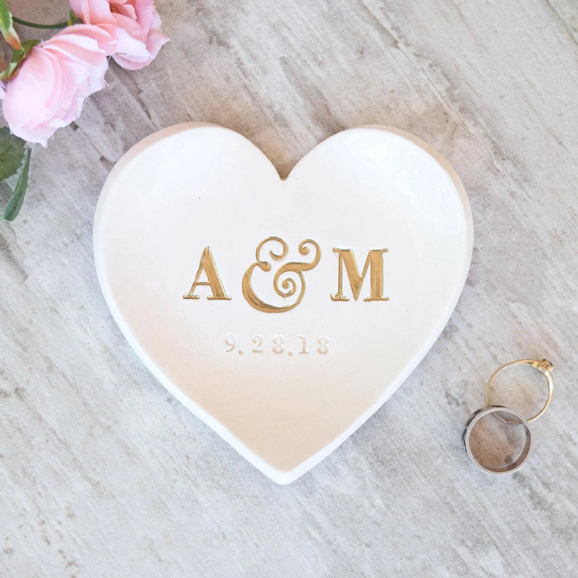 handmade ceramic custom pottery heart shaped plate with typographic design on white surface. Large 5 inch heart tray with hand stamped clay: 2 name monogram initials and date. Unique heirloom engagement ring holder bridal couple keepsake. The initials are painted silver. Ideal for engaged party gift, wedding shower bride to be present, future daughter son in law memento. Useful jewelry storage tabletop decorative tray for dresser, bedside table, or by a sink.