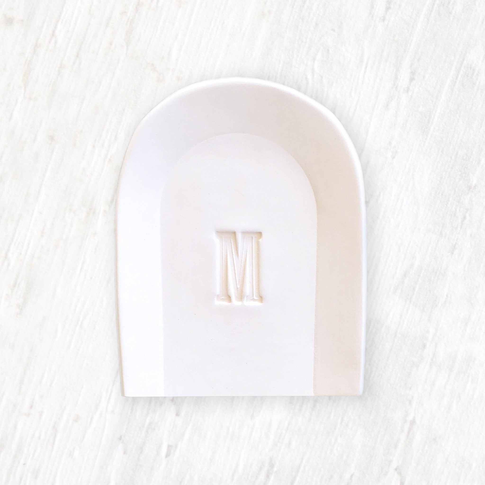 handmade ceramic large spoon rest with pressed letter M in clay on wood surface. Modern white custom pottery utensil holder kitchen dish, stove top cook aid, spoon rester tray.